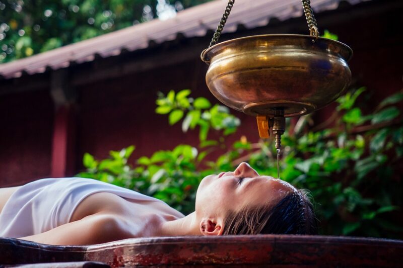 ayurveda massage alternative healing therapy.beautiful caucasian female getting shirodhara treatment lying on a wooden table in India salon